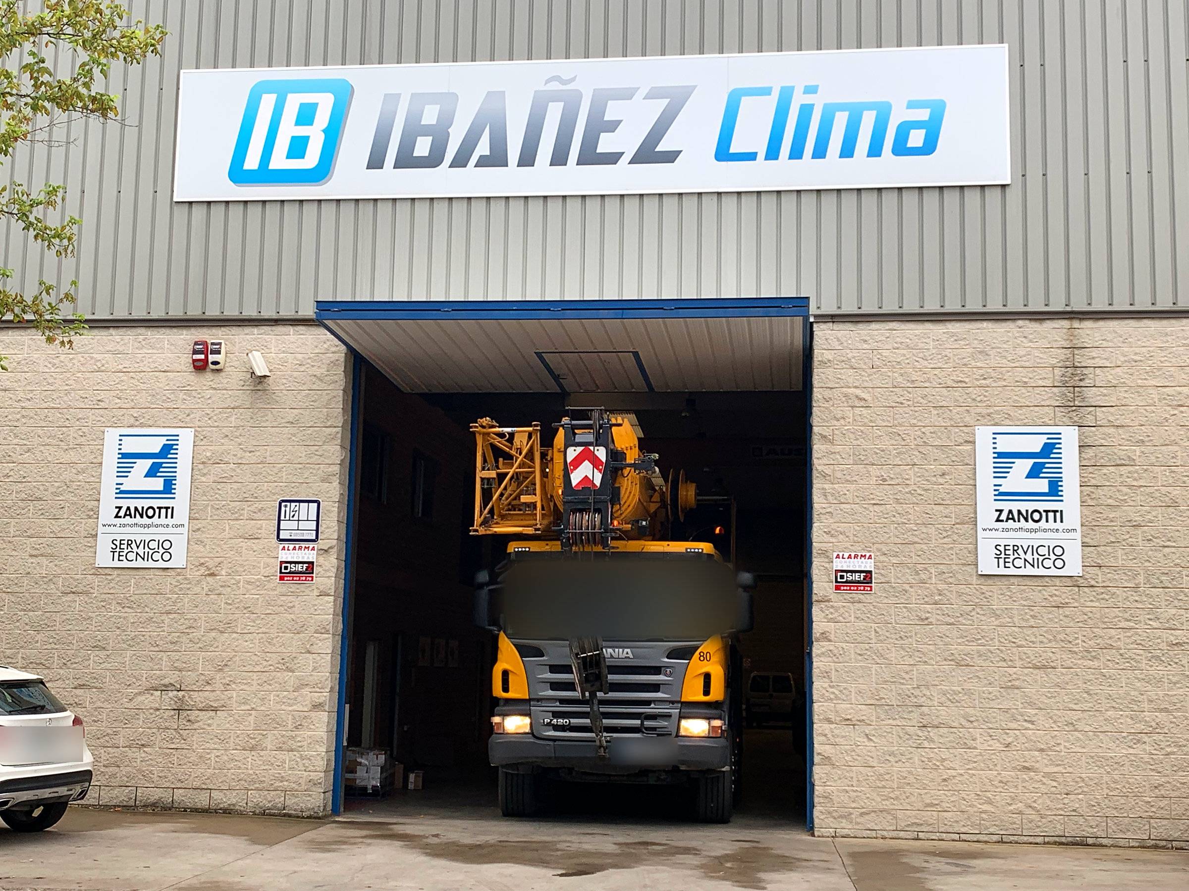 Fachada de la nave de IBAÑEZ CLIMA en Lleida con el rótulo de la empresa y un camión grúa entrando al taller.