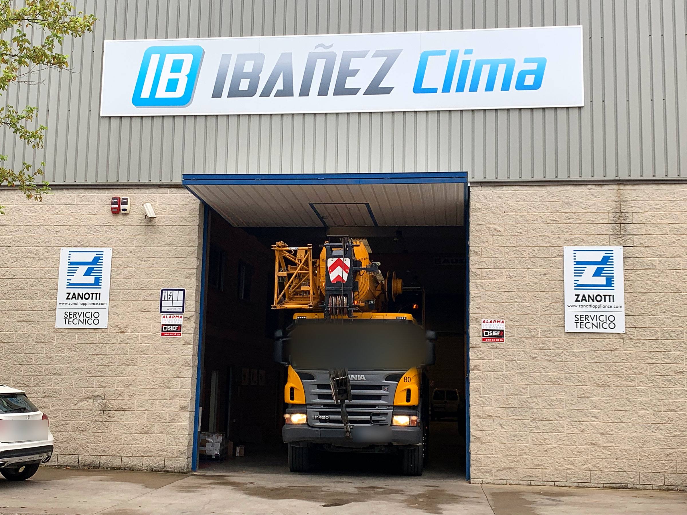 Fachada de la nave de IBAÑEZ CLIMA en Lleida con el rótulo de la empresa y un camión grúa entrando al taller.